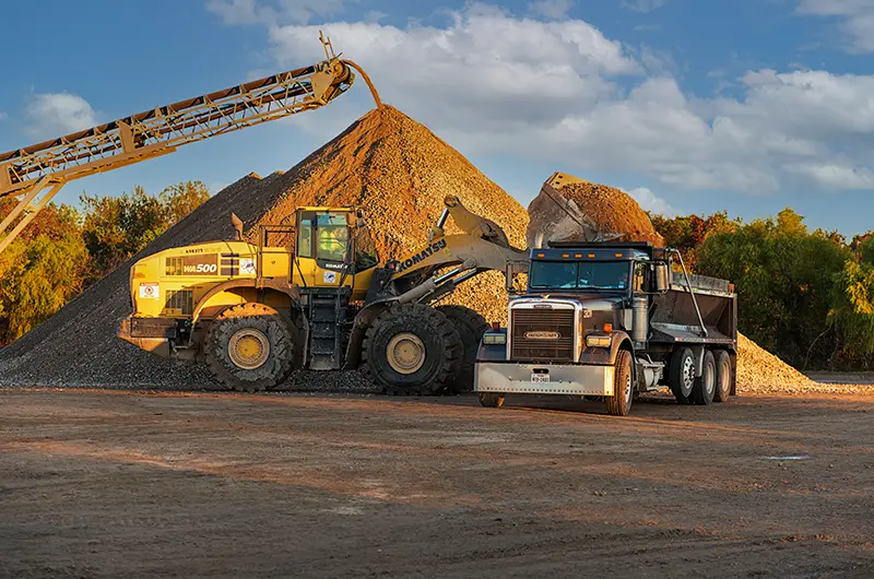 tractors parked in front of a large crushed concrete sand pile